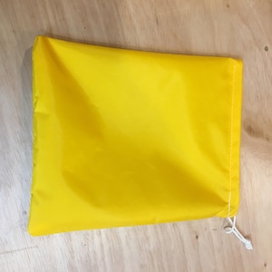 May include: A bright yellow drawstring bag made of fabric. The bag is empty and has a white drawstring.