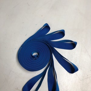 Puede incluir: Un rollo de cinta azul con varios bucles que se extienden desde el rollo. La cinta es un material plano y tejido.