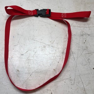 May include: A red adjustable strap with a black plastic buckle. The strap is looped and ready to be attached to something.