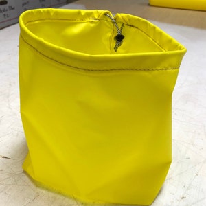 May include: A bright yellow drawstring bag made of a water-resistant fabric. The bag has a black drawstring and a small black toggle.