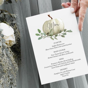 May include: A white pumpkin with green leaves and the word "Menu" written on it. The menu lists a starter, main course, sides, and dessert. The starter is stuffed mushrooms with a blue cheese salad. The main course is pear-thyme brined turkey or herbed chicken with beets and brussels sprouts. The sides are rosemary monkey bread stuffing, French green beans with garlicky almond breadcrumbs, and sweet potato and cauliflower salad. The desserts are pumpkin pie with walnut crust, apple crostata, and pecan pie.