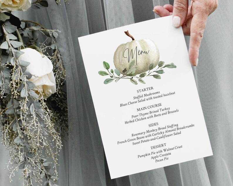 May include: A white pumpkin with green leaves and the word "Menu" written on it. The menu lists a starter, main course, sides, and dessert. The starter is stuffed mushrooms with a blue cheese salad. The main course is pear-thyme brined turkey or herbed chicken with beets and brussels sprouts. The sides are rosemary monkey bread stuffing, French green beans with garlicky almond breadcrumbs, and sweet potato and cauliflower salad. The desserts are pumpkin pie with walnut crust, apple crostata, and pecan pie.