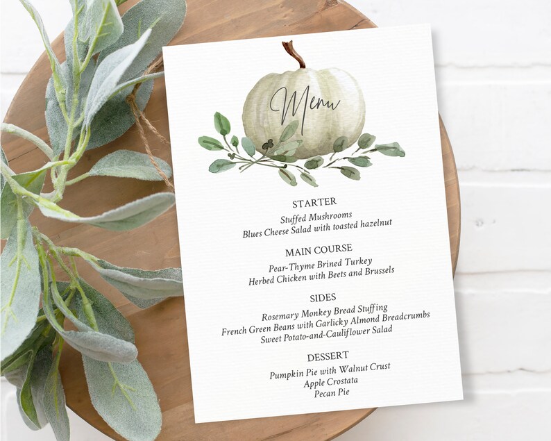 May include: A white pumpkin with green leaves and the word "Menu" written on it. The menu lists a starter, main course, sides, and dessert. The dishes include Stuffed Mushrooms, Pear-Thyme Brined Turkey, Rosemary Monkey Bread Stuffing, and Pumpkin Pie with Walnut Crust.