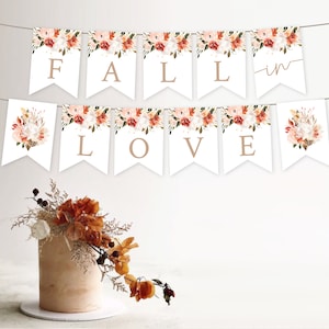 May include: A white banner with floral designs and the words "Fall in Love" in brown lettering. The banner is strung with twine and is hanging from a white wall.