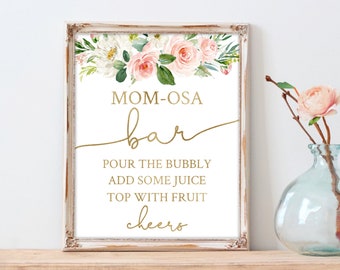 May include: A framed sign with a floral arrangement of pink and white roses and greenery at the top. The sign reads "MOM-OSA bar" in gold script, with instructions below. The frame is a distressed white with gold accents.