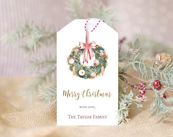 May include: A white Christmas gift tag with a watercolor wreath design. The wreath features ornaments, candy canes, and a red bow. The tag includes the text "Merry Christmas" and "with love, The Taylor Family". A red and white ribbon is attached.