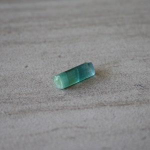 May include: A small, light blue and green crystal with a smooth, polished surface.