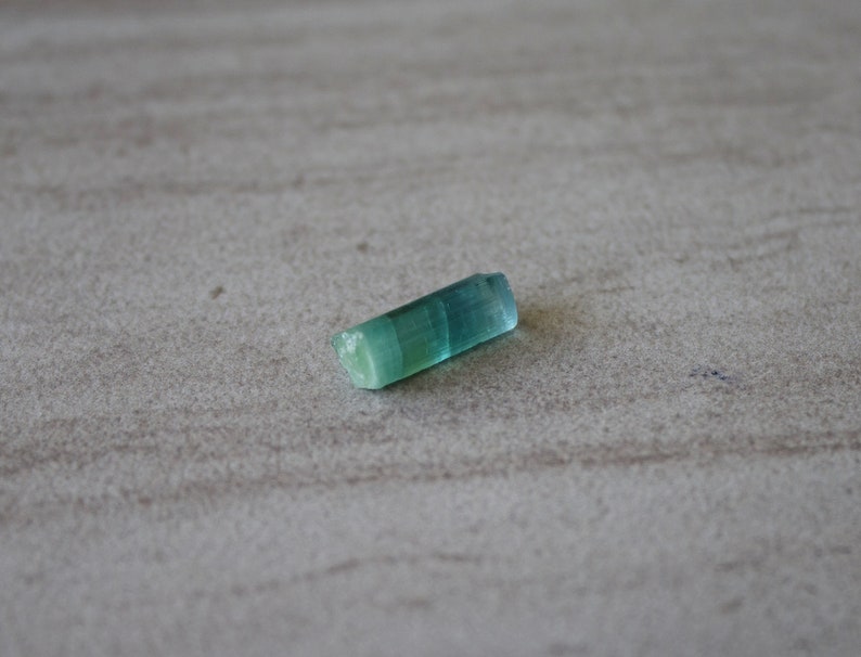 May include: A small, light blue and green crystal with a smooth, polished surface.
