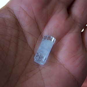 Pode incluir: Um cristal de &aacute;gua-marinha transparente e azul claro com forma retangular. O cristal tem aproximadamente 5 cm de comprimento e est&aacute; na palma da m&atilde;o.