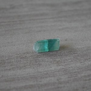 May include: A small, light green crystal with a slightly rough surface.