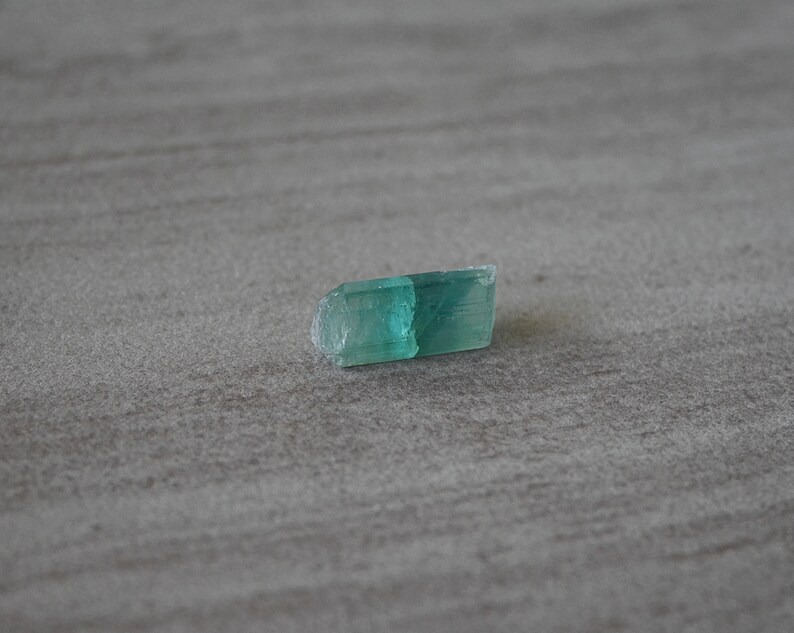 May include: A small, light green crystal with a slightly rough surface.