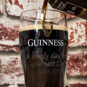 May include: A pint glass of Guinness being poured, with the Guinness logo and text "A lovely day for Guinness Dad Love Beth" etched on the glass. The dark stout is being poured from a bottle.