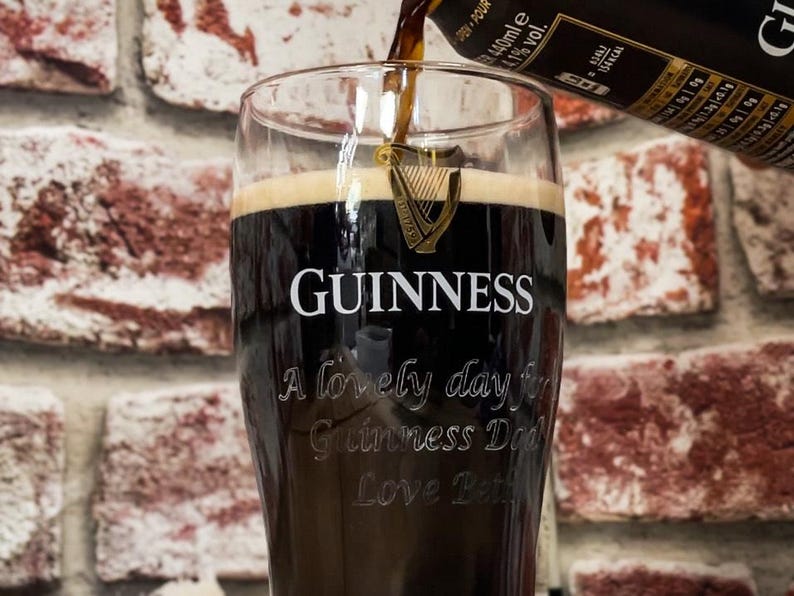 May include: A pint glass of Guinness being poured, with the Guinness logo and text "A lovely day for Guinness Dad Love Beth" etched on the glass. The dark stout is being poured from a bottle.