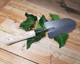 May include: A wooden-handled gardening trowel with a gray metal blade. The handle is engraved with the text "Steve's Trowel".
