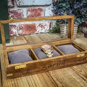 May include: A wooden watch box with a glass top and three compartments. The box is engraved with the name "Karim".
