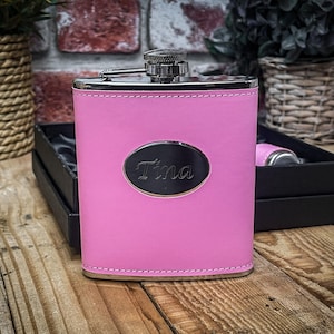 May include: A pink leather-covered flask with a silver top and a silver oval plate with the name "Tina" engraved on it.