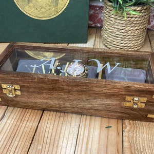 May include: A wooden watch box with a glass top and brass hinges. The box is engraved with the initials "A.J.W.".