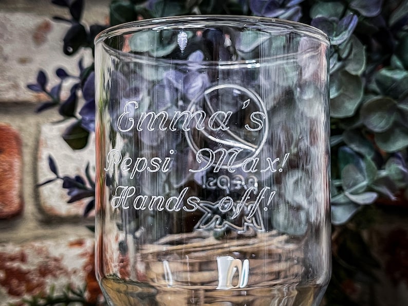 May include: A clear glass cup with the text "Emma's Pepsi Max! Hands off!" etched into the side.