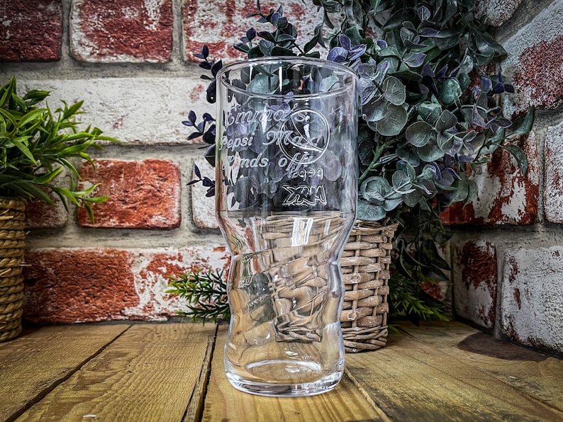 May include: A clear glass with a textured design. The glass has an inscription that reads "Enjoy the Pepsi that makes life a little bit sweeter".