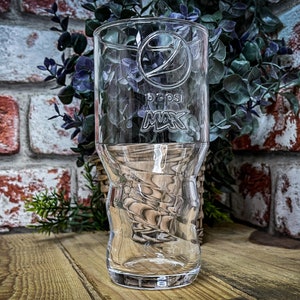 May include: A clear glass with a twisted design and the Pepsi logo etched on the side. The glass is sitting on a wooden surface.