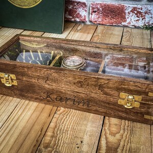 May include: A wooden watch box with a glass top and brass clasps. The box is engraved with the name "Karim".
