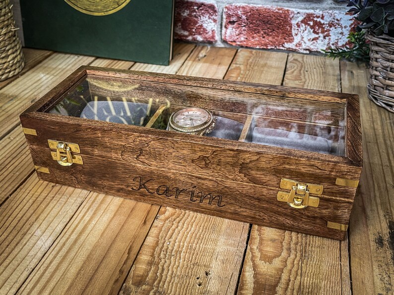 May include: A wooden watch box with a glass top and brass clasps. The box is engraved with the name "Karim".