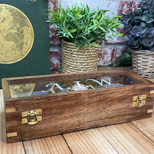 May include: A wooden watch box with a glass top and brass clasps. The box is engraved with the letters "A.I.W."