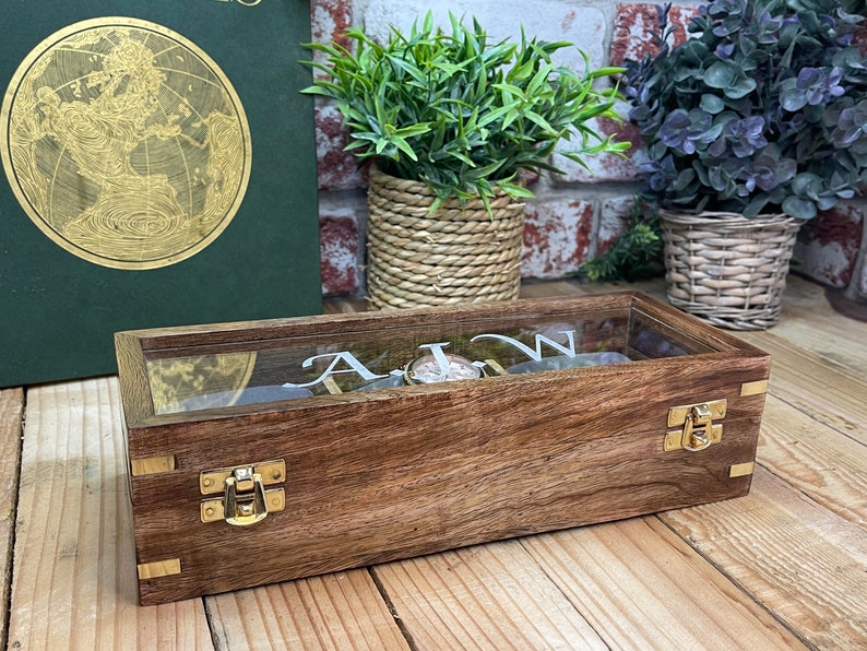 May include: A wooden watch box with a glass top and brass clasps. The box is engraved with the letters "A.I.W."