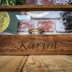 May include: A wooden watch box with a glass top. The box is engraved with the name "Karim".