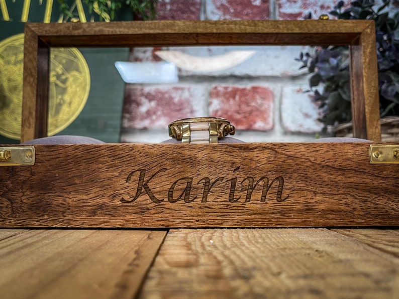May include: A wooden watch box with a glass top. The box is engraved with the name "Karim".
