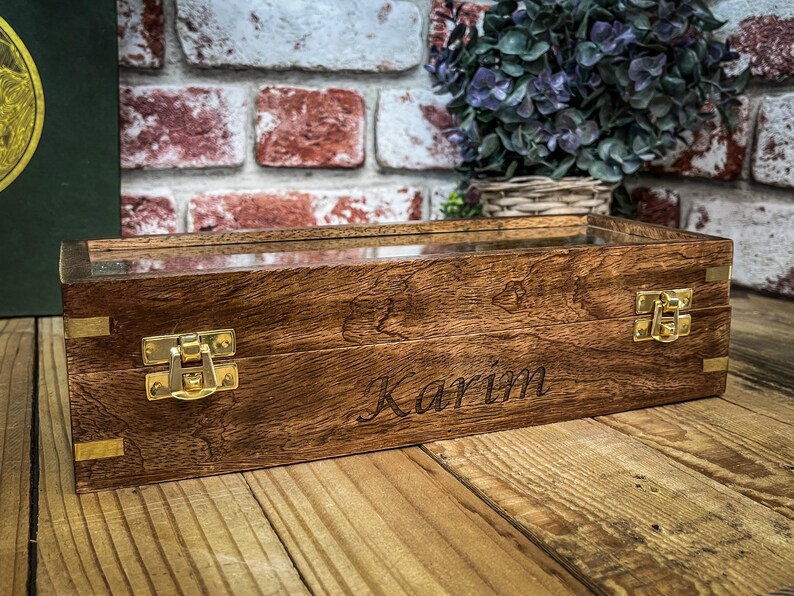 May include: A wooden box with a glass top and brass hinges. The box is engraved with the name "Karim".