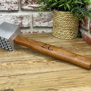 May include: A meat mallet with a wooden handle and a metal head with a textured surface. The handle is engraved with the initials "Z.C."