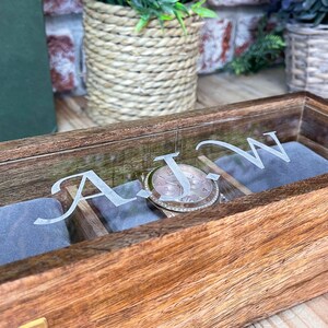 May include: A wooden watch box with a glass lid. The box has a grey velvet interior and is engraved with the initials "A.J.W.".