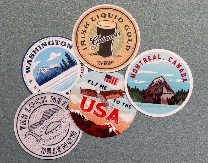 May include: A collection of round stickers featuring travel-themed designs. One sticker displays a pint of Guinness with "Irish Liquid Gold." Others showcase "Washington," "The Loch Ness Monster," "Fly Me to the USA," and "Montreal, Canada."