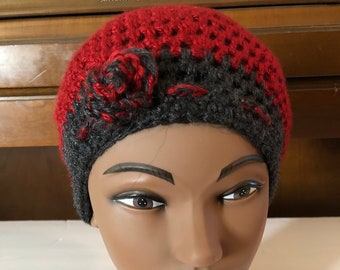 May include: A red and gray crocheted beanie with a flower detail on top.