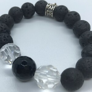 May include: A bracelet made of black lava stone beads, clear faceted beads, and a single black bead. It includes a silver-coloured spacer bead with an ornate design. The beads are strung on elastic.