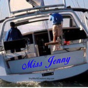 May include: A white sailboat with the name "Miss Jenny" written in blue cursive on the back. The boat is in the water and there are two people on board.