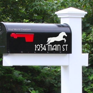 May include: Black mailbox with a red flag and white lettering. The mailbox has a white silhouette of a horse jumping and the address "1234 MAIN ST". The mailbox is mounted on a white post.