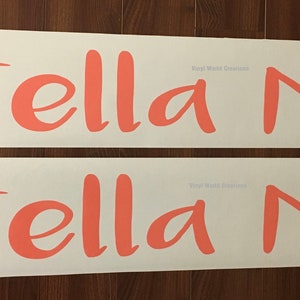 May include: Two white vinyl sheets with the names "Stella Mia" written in a cursive font in a coral pink color.