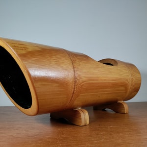 May include: A natural bamboo planter with a rounded shape and a wide opening. The planter has three legs and is made of natural bamboo.