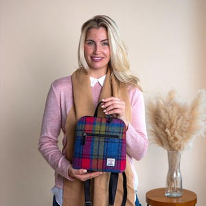 May include: A colorful plaid backpack with a top handle and a zippered front pocket. The backpack features a mix of red, blue, green, and yellow hues. It has black straps and a small label on the front. The bag is approximately 10 inches tall and 8 inches wide.