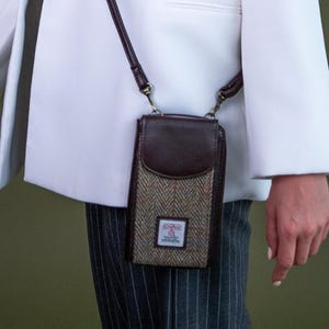 May include: A woman in a white double-breasted blazer with a small brown and tweed crossbody bag. The bag features a dark brown leather top and strap. The background is a solid olive green.