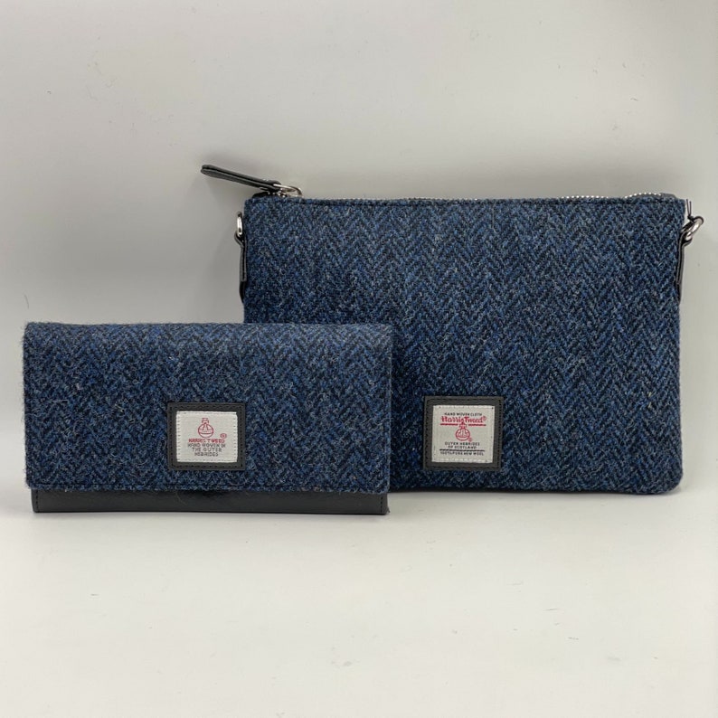 Op de afbeelding: Een blauwe tweed portemonnee en een bijpassende blauwe tweed crossbody tas met een ritssluiting. Beide items hebben een klein rood-wit label met de tekst "Harris Tweed" en een kleine afbeelding van een vogel.