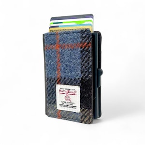 May include: A Harris Tweed wallet with a blue, black, and orange plaid pattern. The wallet is filled with several credit cards. The label reads "Hard Woven Cloth Harris Tweed Outer Hebrides of Scotland 100% Pure New Wool."