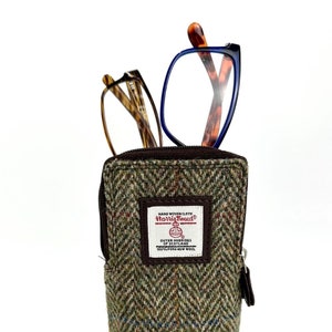 Könnte beinhalten: Ein Brillenetui aus braunem Tweed mit Reißverschluss. Das Etui hat ein Etikett mit der Aufschrift "HAND WOVEN CLOTH HARRIS TWEED OUTER HEBRIDES OF SCOTLAND 100% PURE NEW WOOL". Zwei Brillenpaare ragen aus der Oberseite des Etuis heraus.