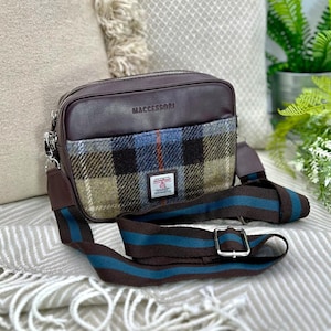 Peut inclure: Un sac bandoulière marron avec un motif à carreaux et une bandoulière rayée. Le sac a un dessus en cuir et le mot "MACESSORI" est imprimé sur le dessus. La bandoulière est marron avec des rayures bleu sarcelle. Une petite étiquette est cousue sur le devant du sac.