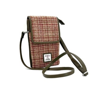 May include: A red and white tweed crossbody phone bag with a green adjustable strap. The bag has a flap closure and a small rectangular patch with the text "Made with Love, Mostly Tweed" on the front.