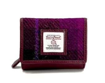 May include: A purple and black plaid wallet with a brown leather trim. The wallet has a label that reads "Hand Woven Cloth Harris Tweed Outer Hebrides of Scotland 100% Pure New Wool."