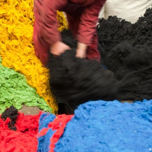 Op de afbeelding: Een assortiment van kleurrijk garen in groen, geel, blauw en rood. Het garen is hoog gestapeld en lijkt van natuurlijke vezels te zijn gemaakt.