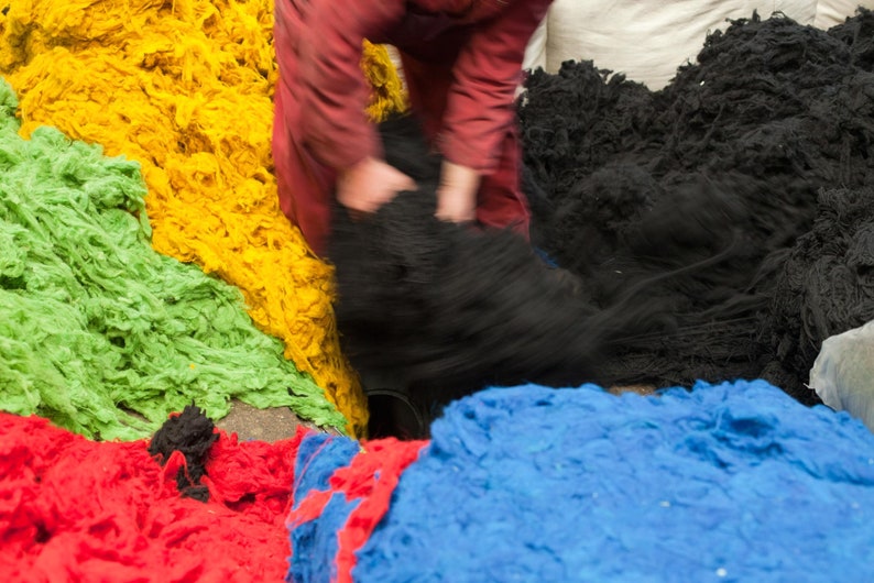 Op de afbeelding: Een assortiment van kleurrijk garen in groen, geel, blauw en rood. Het garen is hoog gestapeld en lijkt van natuurlijke vezels te zijn gemaakt.